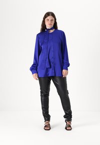 Blå satin langermet skjorte med knappelukking og slips, kombinert med svarte tettsittende skinnbukser og svarte sandaler med stropper.