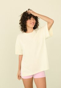 Světle žluté oversized tričko s krátkým rukávem a kulatým výstřihem, vyrobené z hladké látky. Nosené s růžovými šortkami.