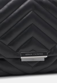 Black quilted leather handbag with chevron pattern, featuring a silver Armani Exchange logo plaque and sleek closure detail.