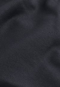 Sort stof med en struktureret overflade og et subtilt ribbet mønster, der viser fleksibilitet og glans under lys.