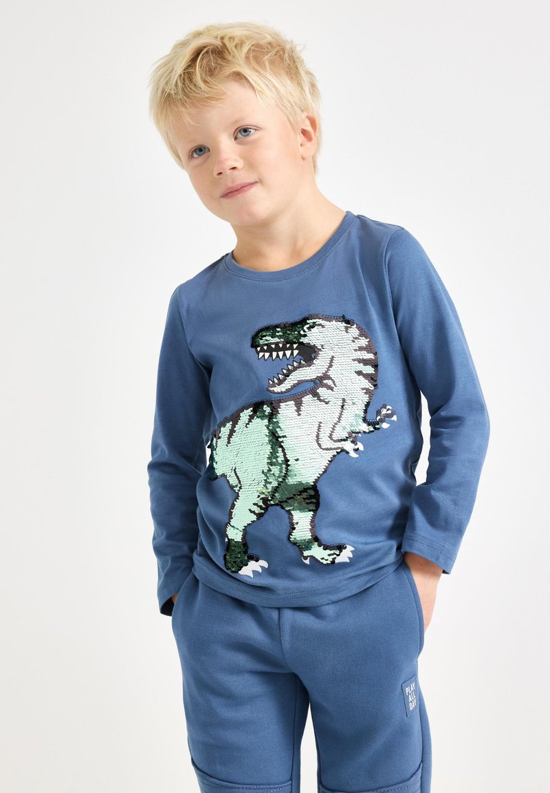 Blaues Langarmhemd mit einem Pailletten-Dinosaurierdesign in Grün und Schwarz. Weicher Stoff mit passenden blauen Hosen. Lässiges Kinderoutfit.