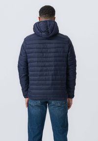 Marineblå quiltet pufferjakke med hætte, der har vandret syninger og en glat tekstur, parret med blå jeans i en afslappet pasform.