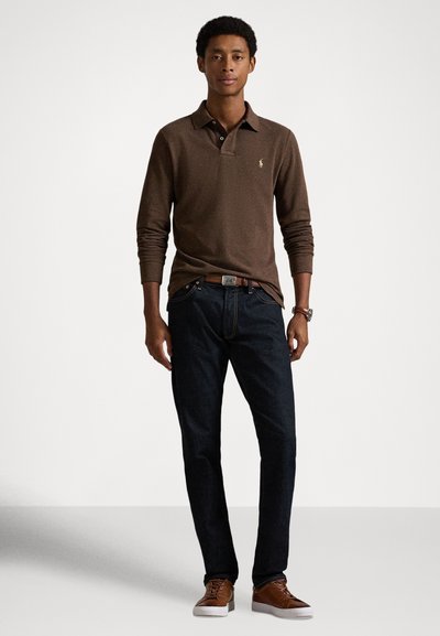 Brūns garām piedurknēm polo krekls ar apkakli, tumši džinsi un brūnas sporta kurpes. Krekls ir ar nepamanāmu logotipu un teksturētu materiālu.