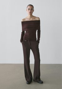 Off-the-shoulder, long-sleeve top in dark brown fabric, paired with matching trousers featuring a button detail. Smooth texture, relaxed fit.