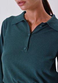 Polo shirt a maniche lunghe turchese con patta con bottoni, design con colletto e texture morbida. Presenta due bottoni e una silhouette aderente.