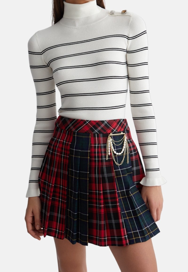 Hvid ribbet turtleneck sweater med sorte striber, parret med en rød og marineblå skotsk ternet plisseret nederdel med en kædeaccessory og dekorative knapper.