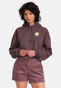 Cropped purple sweatshirt with a front pocket and RVCA logo, paired with corduroy pink shorts featuring vertical stripes and a button closure.
