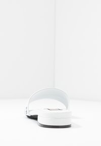 White slide sandal with a flat sole, open toe, and smooth upper strap; minimal design with black accents on the sole's edge.