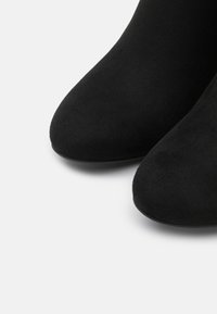 Bottines noires en tissu doux et texturé avec un bout arrondi. Le design présente une surface lisse et élégante ainsi qu'une silhouette simple.