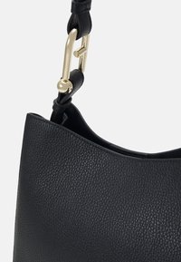 Sac à main en cuir noir avec une finition texturée, présentant un dessus lisse et courbé et du matériel en métal doré sur la bandoulière.