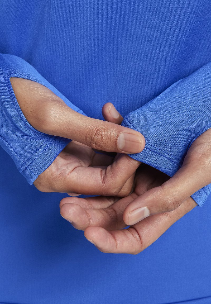Camisa deportiva azul de manga larga con puños de orificio para el pulgar. Primer plano de manos ajustando la manga con tela suave, elástica y que absorbe la humedad.