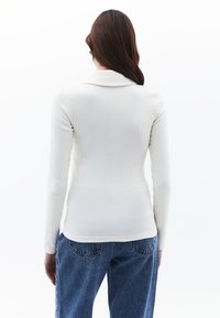 Biała, prążkowana, długi rękaw bluzka z kołnierzykiem, dopasowany krój oraz fakturowany materiał. Połączona z luźnymi niebieskimi dżinsami.