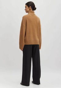 Übergröße brauner Rollkragenpullover aus weichem Stoff mit geripptem Saum und Bündchen, kombiniert mit schwarzen weiten Hosen.