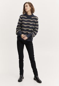 Chunky gebreid sweater in marineblauw met beige golfstrepen, ribbelkraag en manchetten. Gecombineerd met zwarte slim-fit broek en zwarte enkellaarsjes.