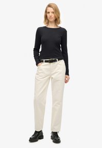 Czarna bluzka z długim rękawem, białe spodnie, czarny pasek i czarne botki sznurowane. Zarówno spodnie, jak i bluzka mają dopasowany krój i jednolite kolory.