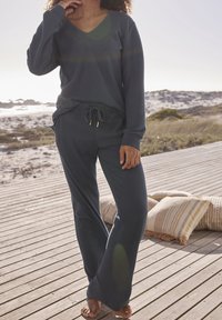 Szary, prążkowany zestaw odzieży domowej składający się z długiego rękawa topu z dekoltem w kształcie V oraz spodni na sznurku. Tkanina ma miękką fakturę i luźny krój.