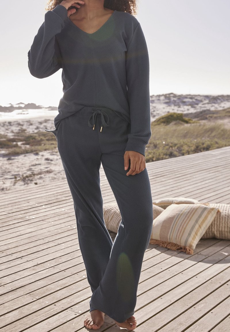 Szary, prążkowany zestaw odzieży domowej składający się z długiego rękawa topu z dekoltem w kształcie V oraz spodni na sznurku. Tkanina ma miękką fakturę i luźny krój.
