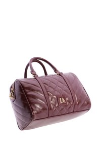 Bolso de mano de cuero acolchado burdeos con doble asa, placa de logo dorado y detalles de cremallera dorados sobre fondo blanco.