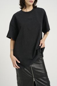Svart oversized t-skjorte med korte ermer, myk stoff, med en teksturert logo. Kombinert med et svart lærskjørt med glidelåsdetalj.