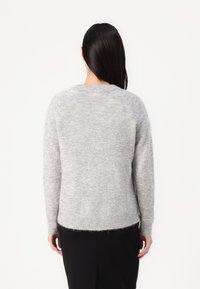 Harmaa neulottu neule, jossa on pehmeä tekstuuri, raglan-hihat ja resorit hihansuissa, hieman kaartuva helma, pidettyMustien housujen päällä.