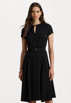 Sort kjole med kap-sleeves, en nøglehul-udskæring og tætsiddende talje, der har et bælte som accent. Stofvalget har en glat tekstur og en svajende nederdel.