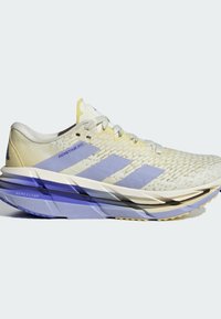 Scarpe da corsa giallo chiaro con una parte superiore testurizzata, strisce viola e una suola spessa multicolore con un design del battistrada a motivi.