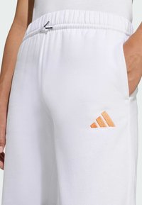 Biele bavlnené teplákové nohavice s elastickým pásom, s malou oranžovou vyšitou značkou na boku a bočnou kapsou.