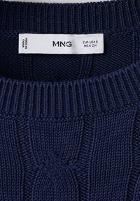 Encolure de pull en maille bleu marine avec étiquette blanche indiquant la marque MNG, taille S pour EUR-USA et CH pour MEX, fabriqué en Chine.