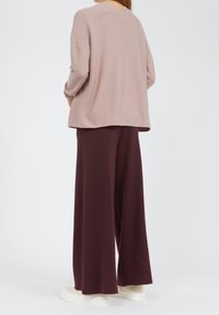 Jasnoróżowy, oversize'owy sweter z fakturowanej tkaniny, zestawiony z luźnymi, ciemnobordowymi spodniami i kremowymi trampkami.