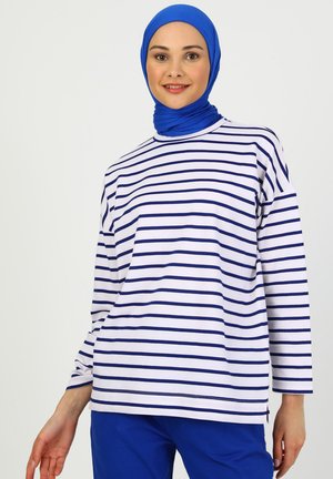 Stribet langærmet top i hvid og marineblå bomuld, med rund halsudskæring og afslappet pasform, parret med blå bukser.