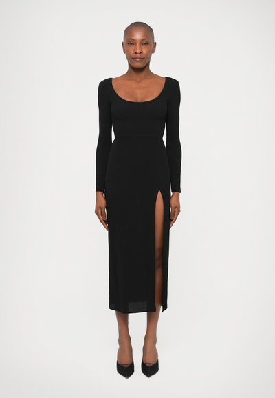 Langes schwarzes Kleid in taillierter Form, mit einem Rundhalsausschnitt und einem hohen Schlitz bis zum Oberschenkel; aus einem glatten, elastischen Material gefertigt.