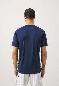 Navy short-sleeve sports shirt with a crew neck and side accents, paired with white athletic shorts. Smooth fabric, no visible logos.