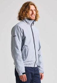 Hellgraue Zip-Jacke mit hohem Kragen, elastischen Bündchen und Saum. Verfügt über zwei Seitentaschen und ein schwarzes Logo auf dem linken Ärmel.