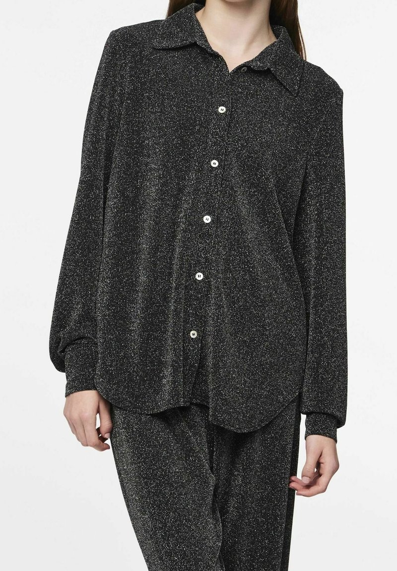 Camicia nera scintillante con colletto e maniche lunghe. Presenta una vestibilità rilassata e una consistenza morbida, abbinata a pantaloni coordinati.