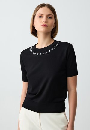 Top en tricot noir à manches courtes avec un col rond, orné de perles décoratives autour du col et d'une finition côtelée ajustée.