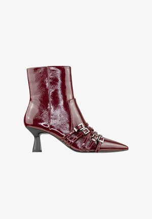 Stivale alla caviglia in pelle patent color bordeaux con punta affusolata, tacco stiletto sottile e diverse cinghie con fibbie argentate sulla parte anteriore. Texture liscia.