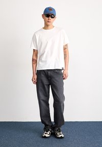 Hvit T-skjorte med korte ermer, svarte denimbukser, og svart-hvite joggesko; en blå baseballcap og solbriller fullfører stilen.
