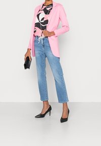 Blazer rosa chiaro sopra una maglia a motivo bianco e nero, abbinata a jeans azzurri a gamba dritta e tacchi neri con punta appuntita. Borsa clutch nera in mano.