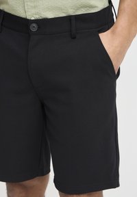 Black shorts made of a textured fabric with a smooth finish. Features a button closure, side pockets, and knee-length cut.