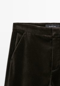 Donkerbruine fluwelen broek met een gladde textuur, zijzakken en een schone tailleband. Label toont "Massimo Dutti."