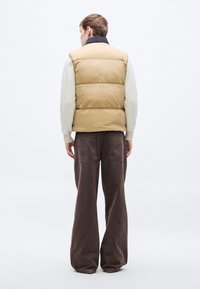 Helekollane turske vest kõrge kraega, kombineeritud heledale kreemja kampsuniga ja lõdva, tumepruuni pükstega. Tekstureeritud, polsterdatud muster.