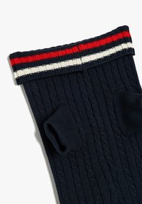 Los calcetines de punto en color navy cuentan con un puño acanalado con franjas rojas, blancas y rojas, y una textura de punto en cable en todo el cuerpo.