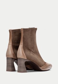 Botas de tobillo de ante marrón con un acento de cuero suave, punta redondeada y tacón apilado texturizado. Cuenta con una cremallera lateral para el cierre.