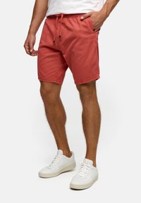 Røde bomullsshorts med elastisk midjebånd og snøring, med sidelommer og en avslappet passform, parret med hvite sneakers.