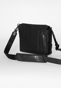 Black messenger bag featuring a combination of smooth leather and fabric, rectangular shape, adjustable strap, and front zipper pocket.