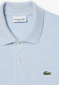 Ljusblå polo t-shirt med ett texturerat tyg, ribbad krage, treknapprad och en broderad grön krokodil-logotyp på bröstet.