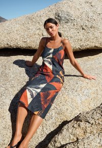 Abito senza maniche con motivo geometrico che presenta tonalità di blu, arancione e crema. Realizzato in tessuto leggero, arriva appena sotto il ginocchio.