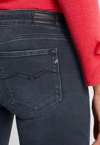 Jeans de color gris oscuro con un acabado texturizado, que cuentan con un bolsillo trasero con un diseño de costura curva y un parche de cuero negro de la marca.