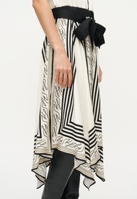 Γυναίκα που φοράει μια φούστα με ασπρόμαυρο σχέδιο, ασύμμετρη στο τελείωμα και με μεγάλο μαύρο φιόγκο δεμένο στη μέση.