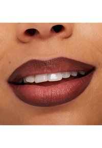 Close-up of a smiling mouth with dark brown matte lipstick and visible white teeth on medium skin tone.